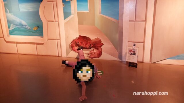 軽井沢トリックアートミュージアムでかにに掴まれている錯覚の絵の前にいる娘の写真